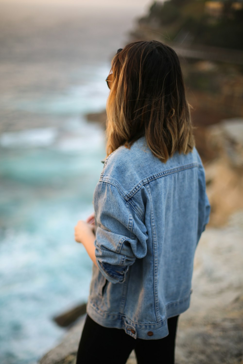 海を眺めるブルーデニムジャケットの女性