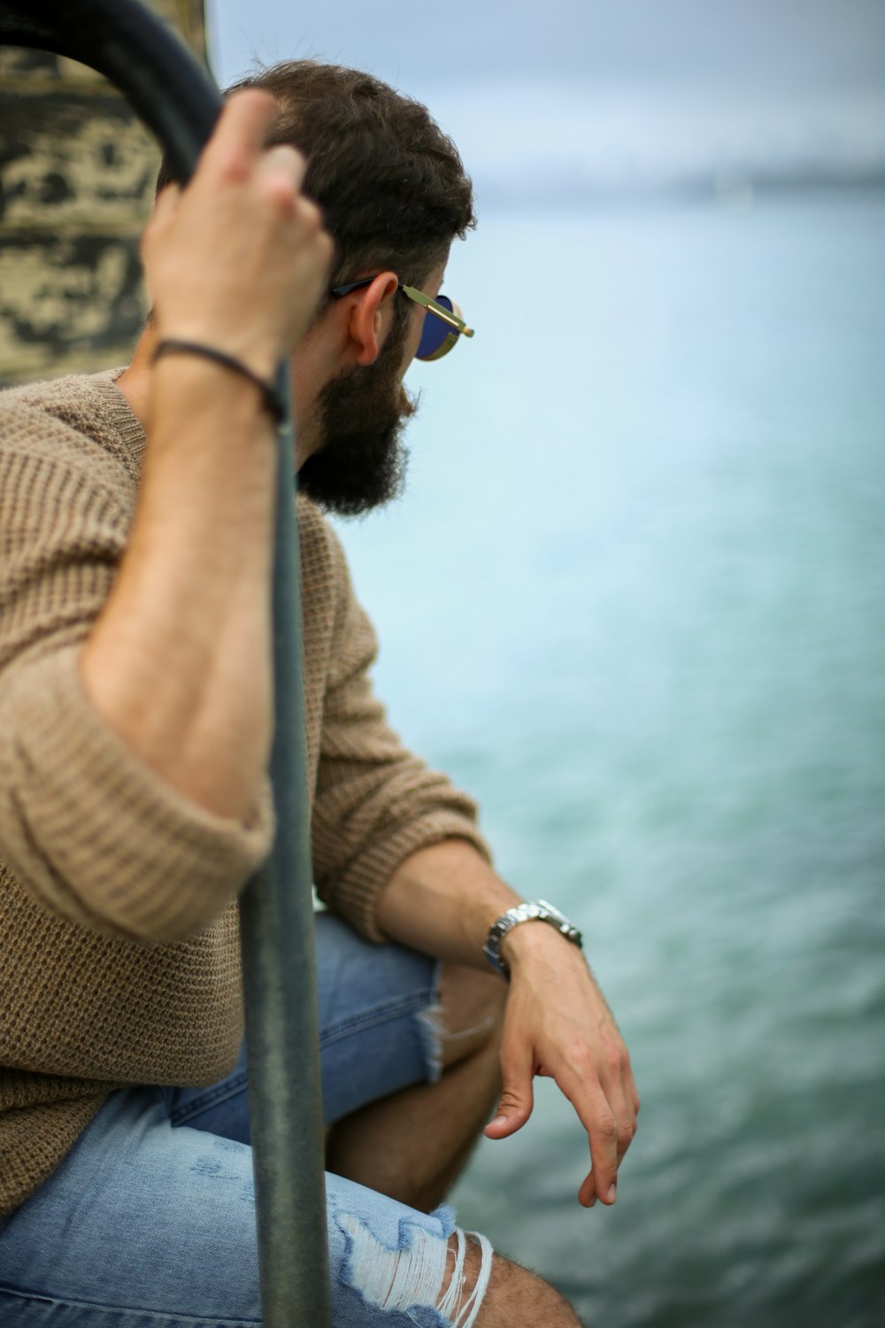 man sitting on while holding metal rail near ocean water