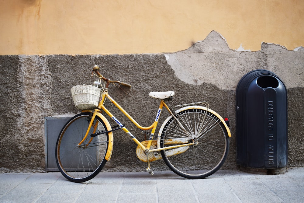 bicycle leaning on wall near trash bin