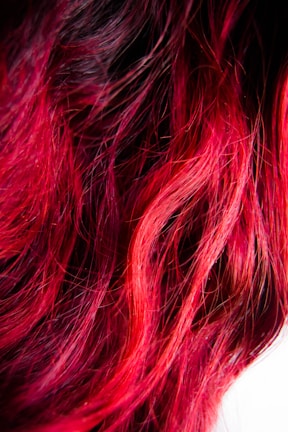 Vibrant strands of hair in shades of red and pink intertwine, creating a rich tapestry of color and texture. The individual strands are illuminated, highlighting their sheen and the dynamic play of light on the surface.