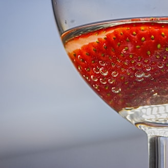 Close-up of a bright red strawberry pastille dissolving in a glass of clear water.