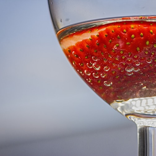 Close-up of a bright red strawberry pastille dissolving in a glass of clear water.