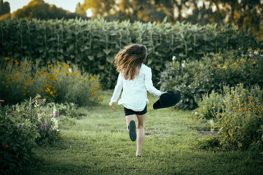 mujer corriendo sobre la hierba rodeada de flores durante el día