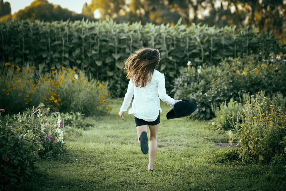 Frau, die tagsüber auf Gras läuft, umgeben von Blumen