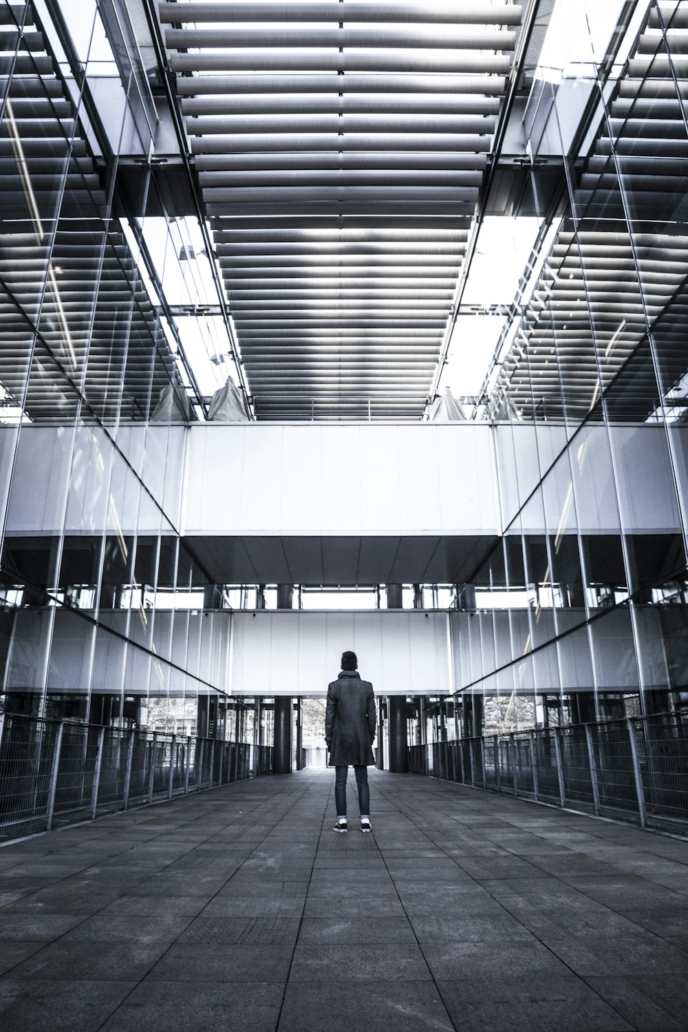 person standing near curtain wall building grayscale photography