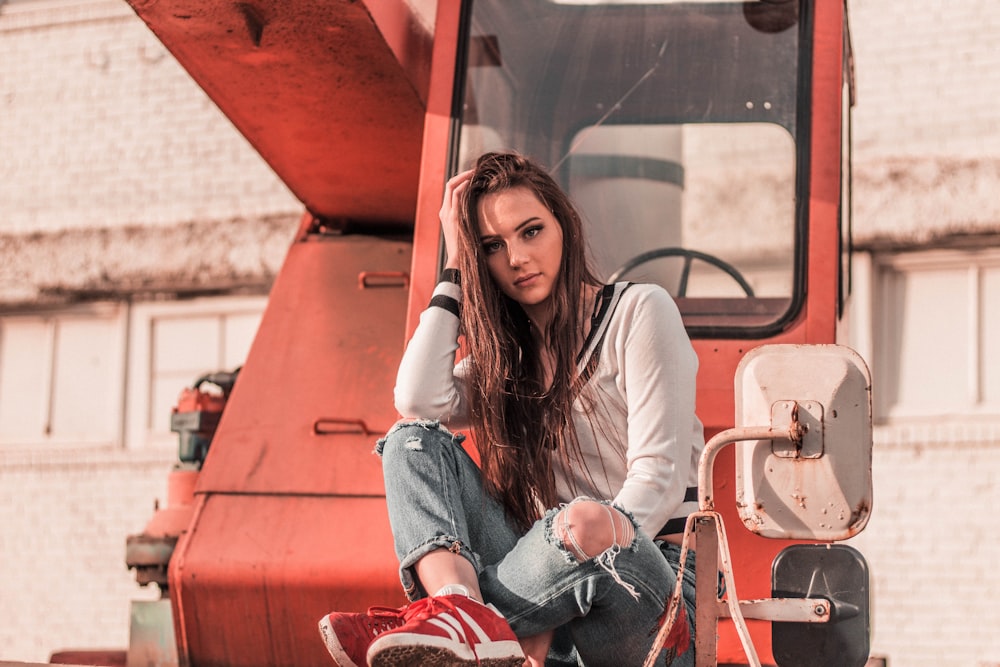 woman sitting in front of red heavy equipment while resting her hand on head