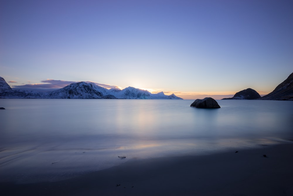 calm body of water near mountain covered with snow