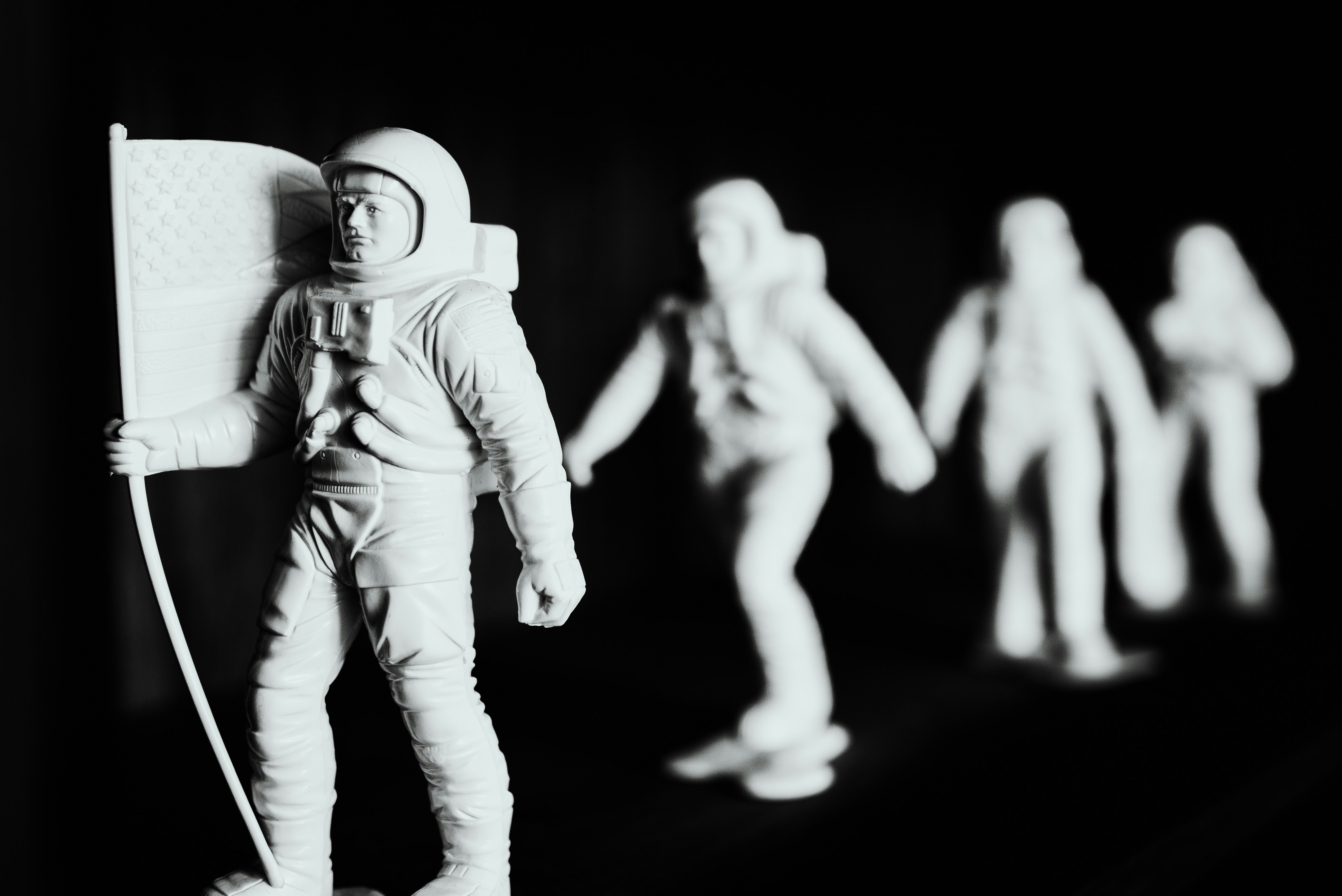 A row of astronaut figurines, the first carries a flag
