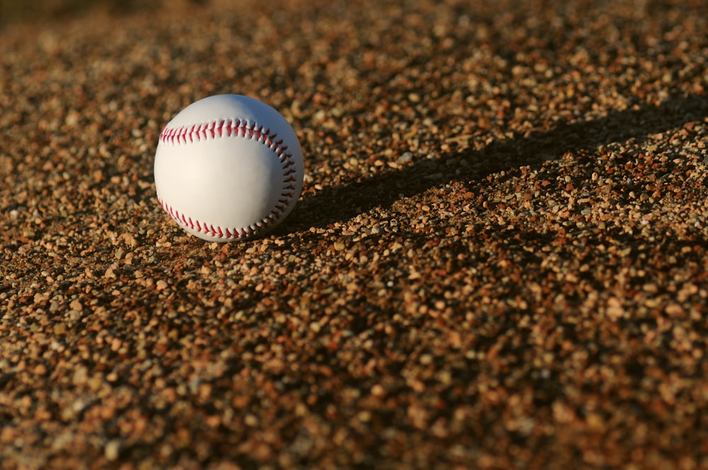 baseball bianco e rosso su terreno marrone durante il giorno