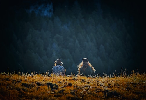 man and woman sitting on brown field