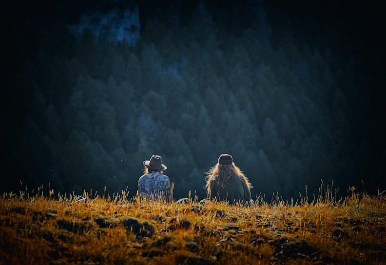 man and woman sitting on brown field