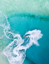 A person riding a jet ski with splashing water and a vibrant coastline background.