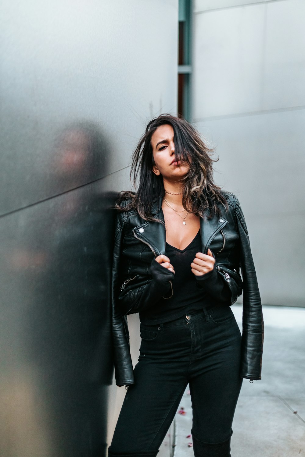 woman touching her black leather jacket while standing near silver wall