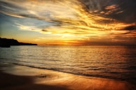 A serene beach in Bali at sunset with golden skies reflecting on calm waters.
