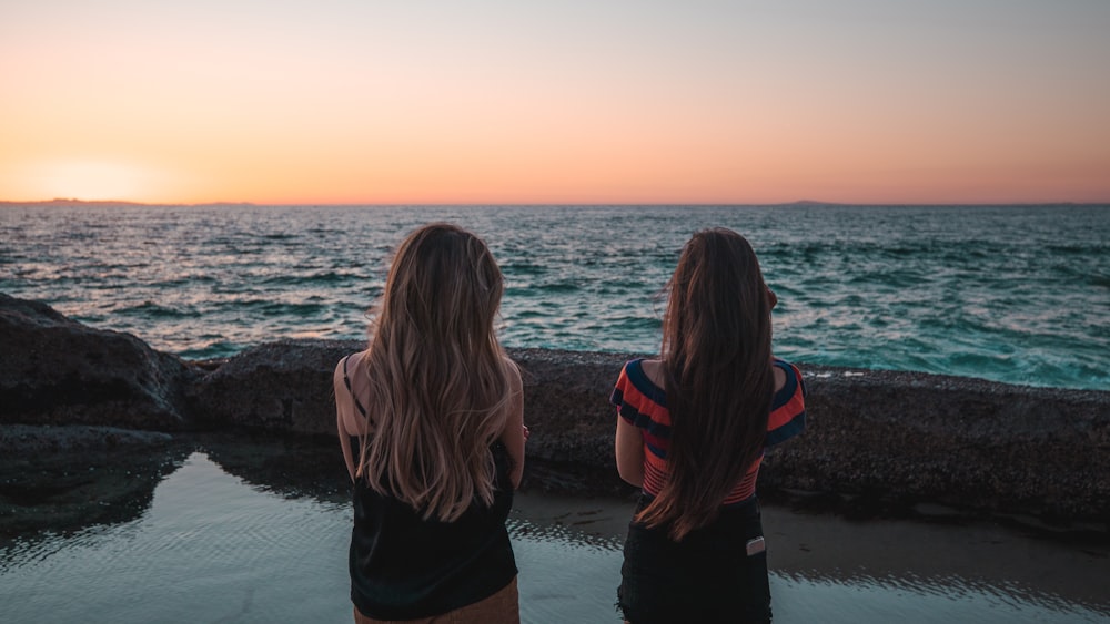 duas mulheres em pé de frente para o corpo de água durante o dia