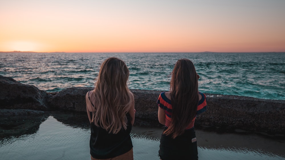 two woman standing facing body of water during daytime