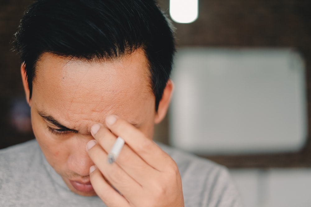 person holding cigarette stick and scratching his face