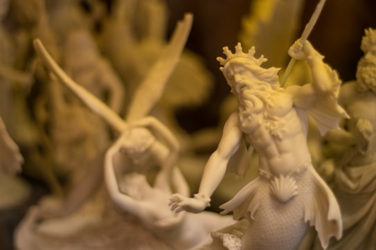 An intricately detailed sculpture depicts mythological figures, including a muscular merman-like deity with a crown and a trident, alongside another figure with outstretched arms. The scene is filled with dynamic movement and artistic craftsmanship.