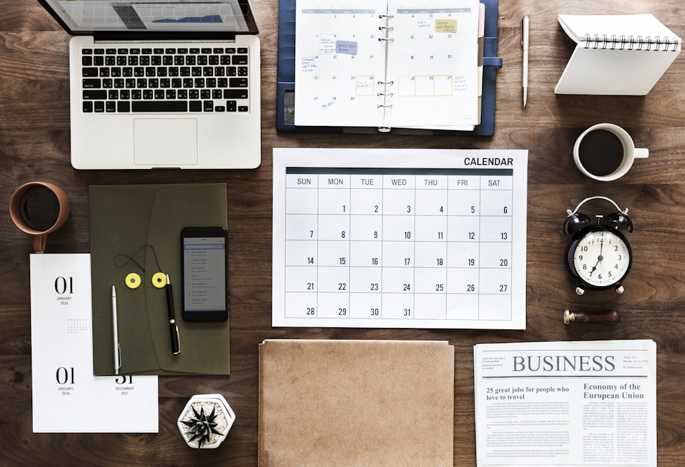 space gray MacBook Pro, Calendar chart, and Business magazine on table