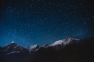 Star-filled sky over majestic mountains with silhouettes of trekkers