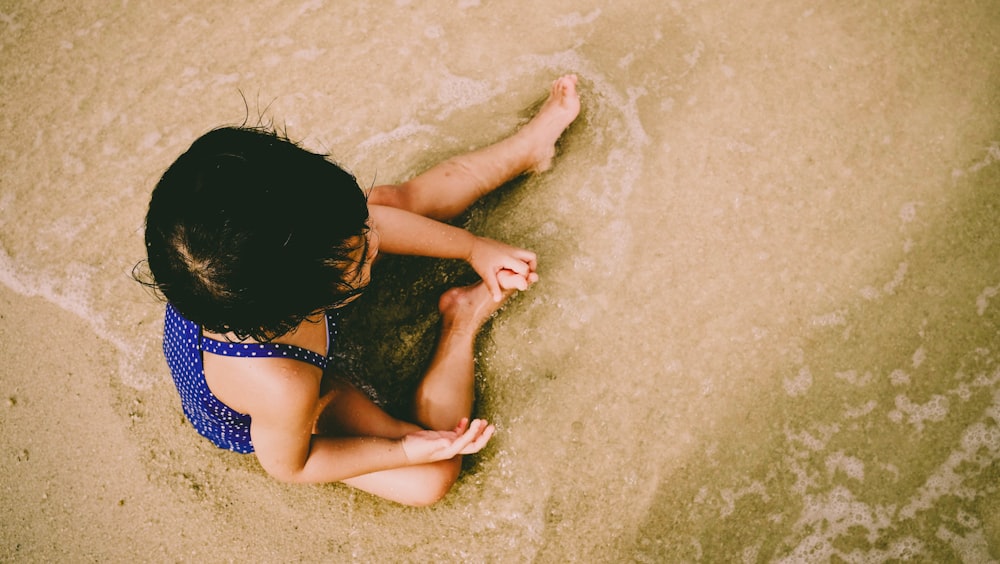 a little girl sitting in the sand on the beach