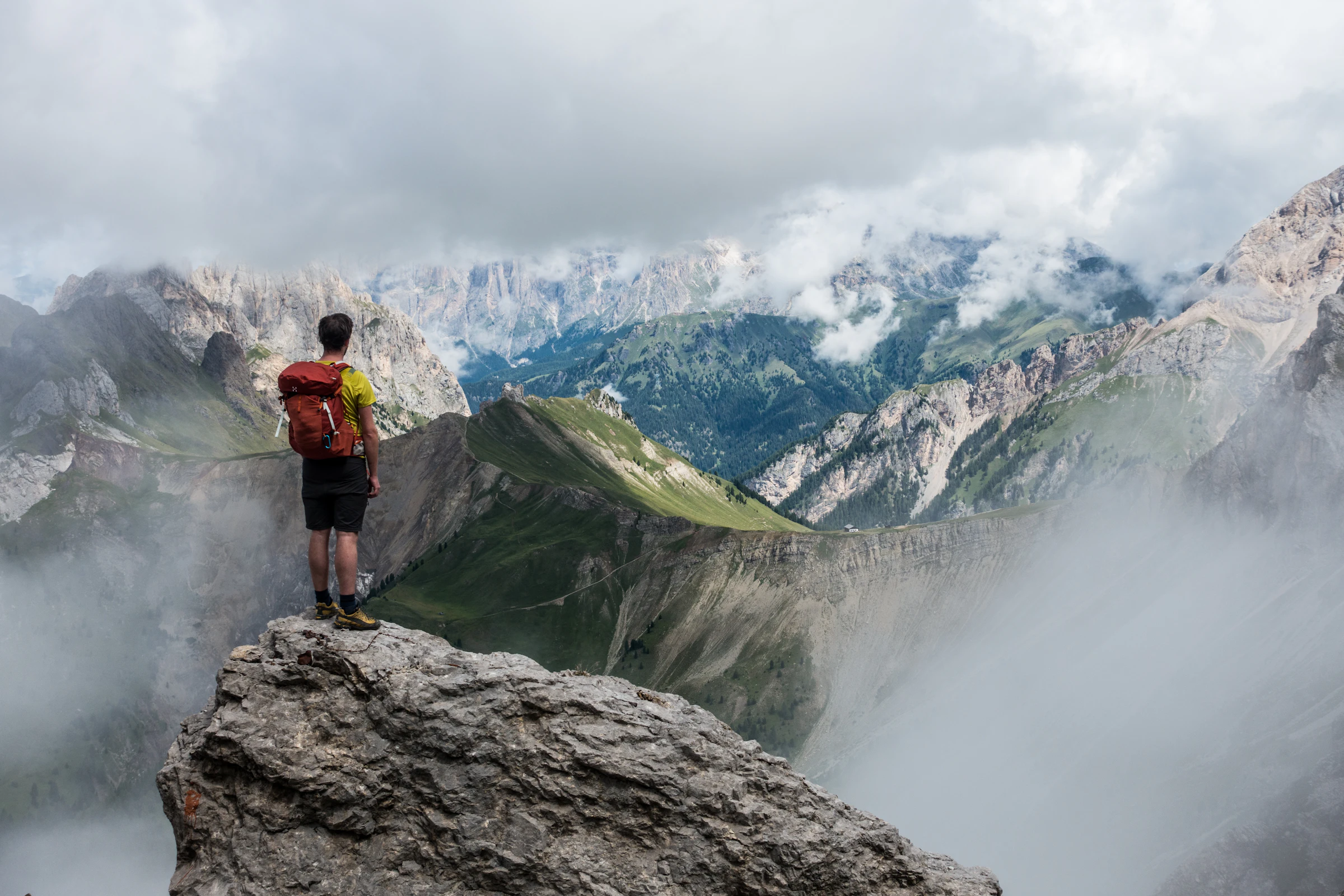 Hiker with a red backpack standing on a rocky ledge overlooking misty mountain peaks