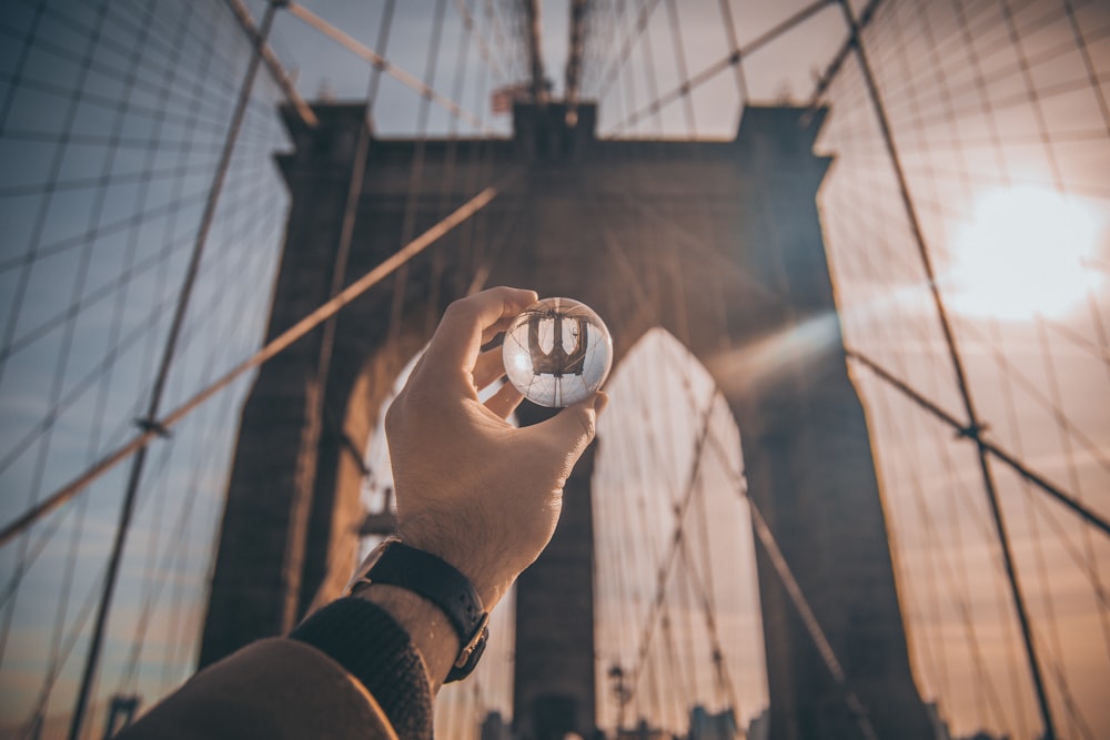 man holding ball facing Brooklyn Bridge, New York
