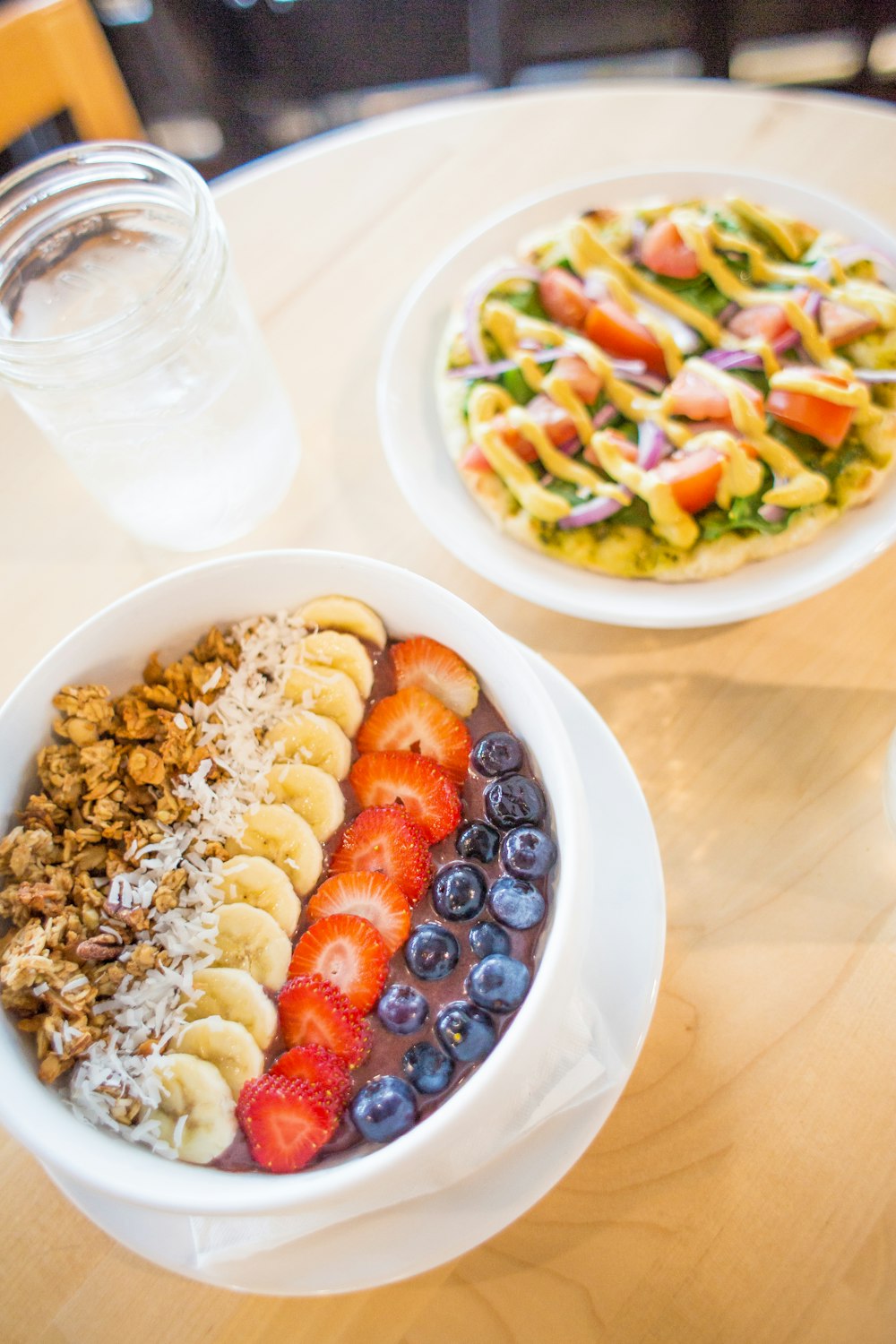 slice banana, strawberry and blueberries on white bowl beside vegetable salad on table