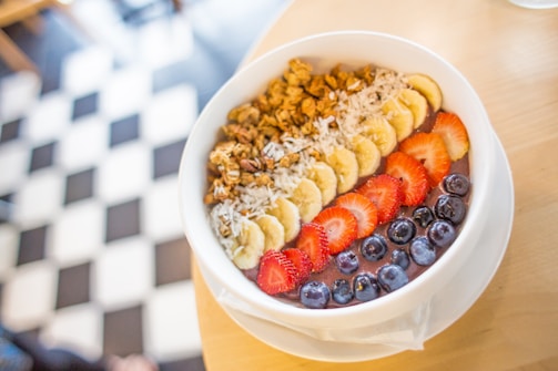 A close-up of a colorful, healthy breakfast bowl with fresh fruits and nuts on a wooden table.