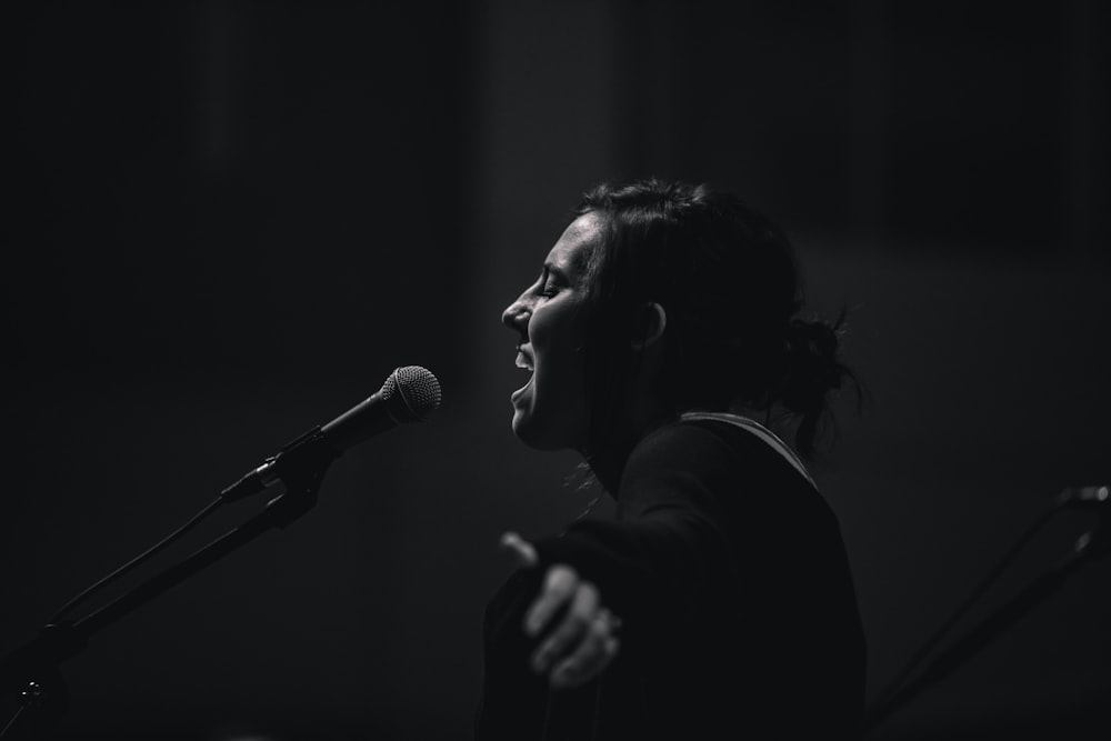 grayscale photo of woman standing beside microphone