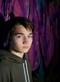 A young person rocking a bold, oversized hoodie with graphic prints, leaning against a graffiti wall.