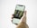 A hand holding a smartphone displaying an Instagram post. The screen shows a photo of two smiling children standing in front of greenery, possibly a garden or park. The person holding the phone is wearing a brown jacket.