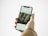 A hand holding a smartphone displaying an Instagram post. The screen shows a photo of two smiling children standing in front of greenery, possibly a garden or park. The person holding the phone is wearing a brown jacket.