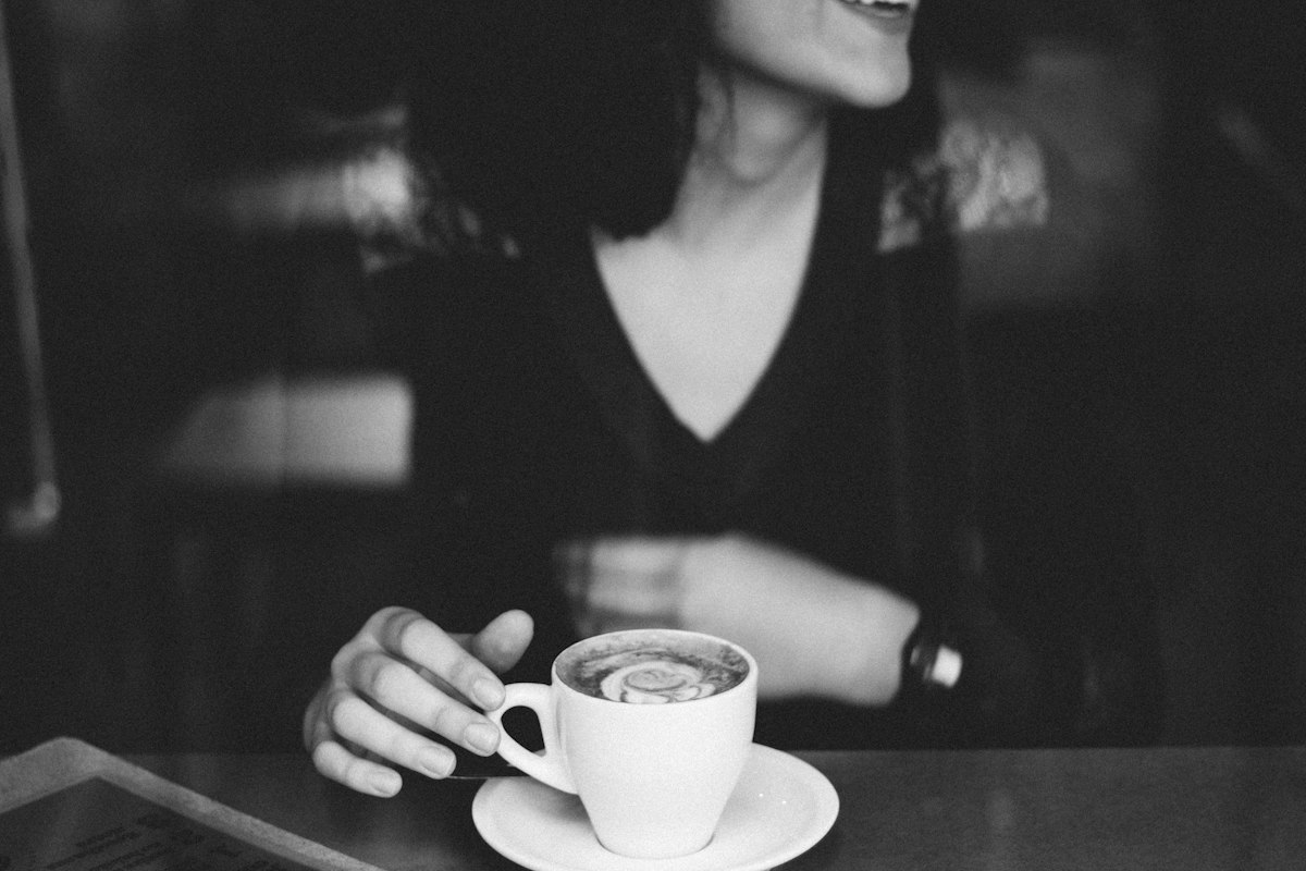 A smiling woman holding a coffee cup by a cafe window