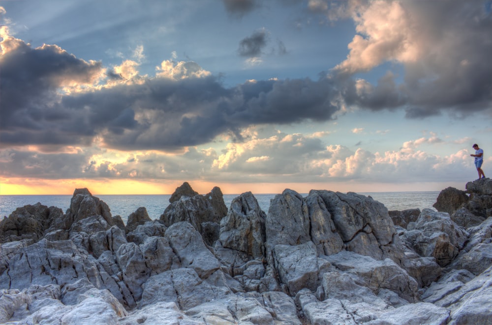 man standing on rock formation near ocean under gray clouds