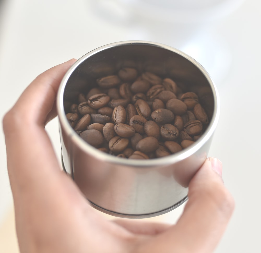 Persona sosteniendo el grano de café en un recipiente de acero inoxidable