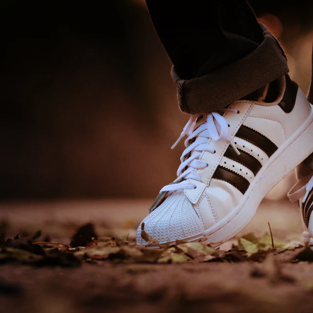 A person wearing a pair of white adidas Superstar sneakers outdoors in daylight