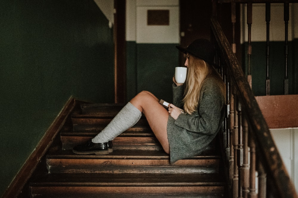 femme assise sur des escaliers en bois brun tout en buvant