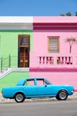 blue sedan parked beside pink and green house