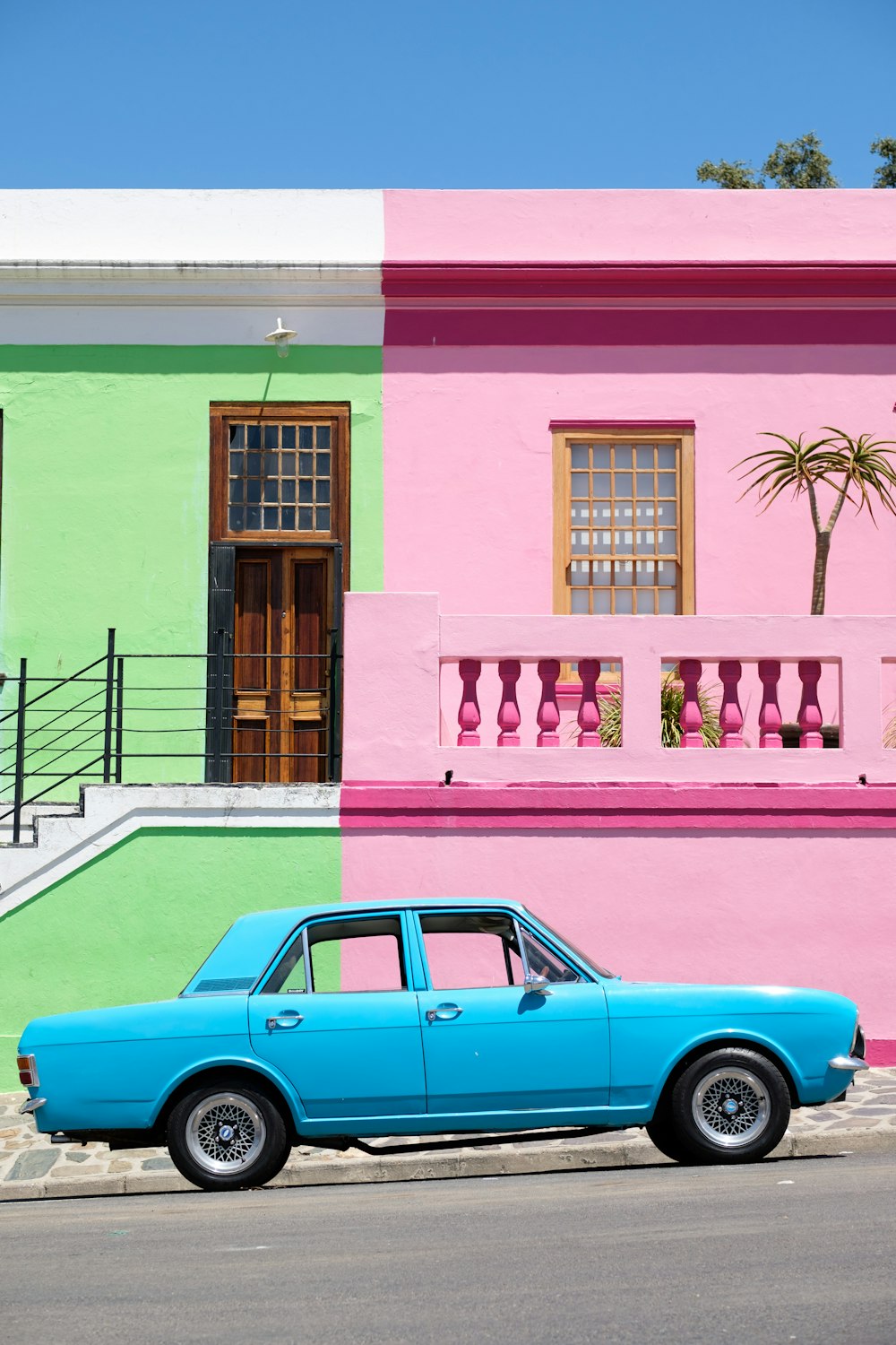 Sedán azul estacionado junto a la casa rosa y verde