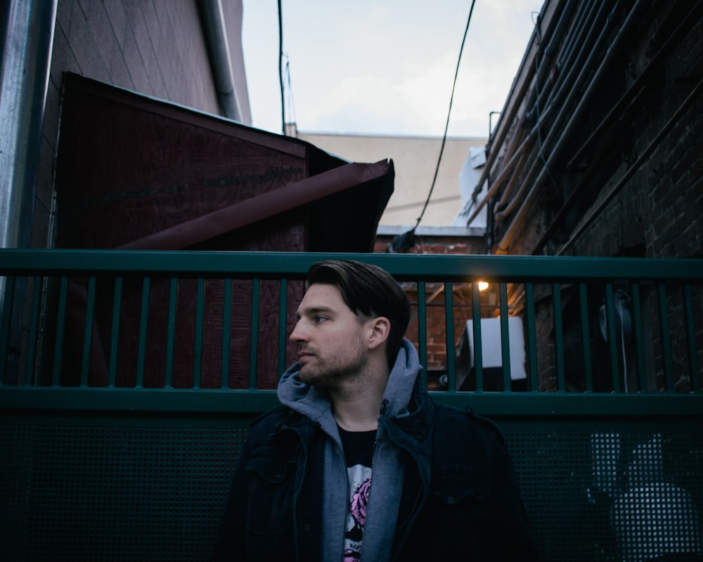 man wearing gray and black pullover hoodie beside green metal gate