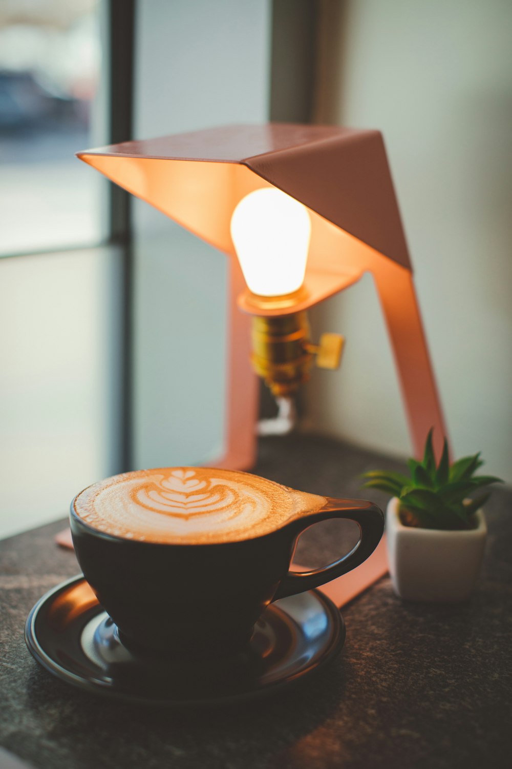 copo de cappuccino perto da lâmpada de mesa