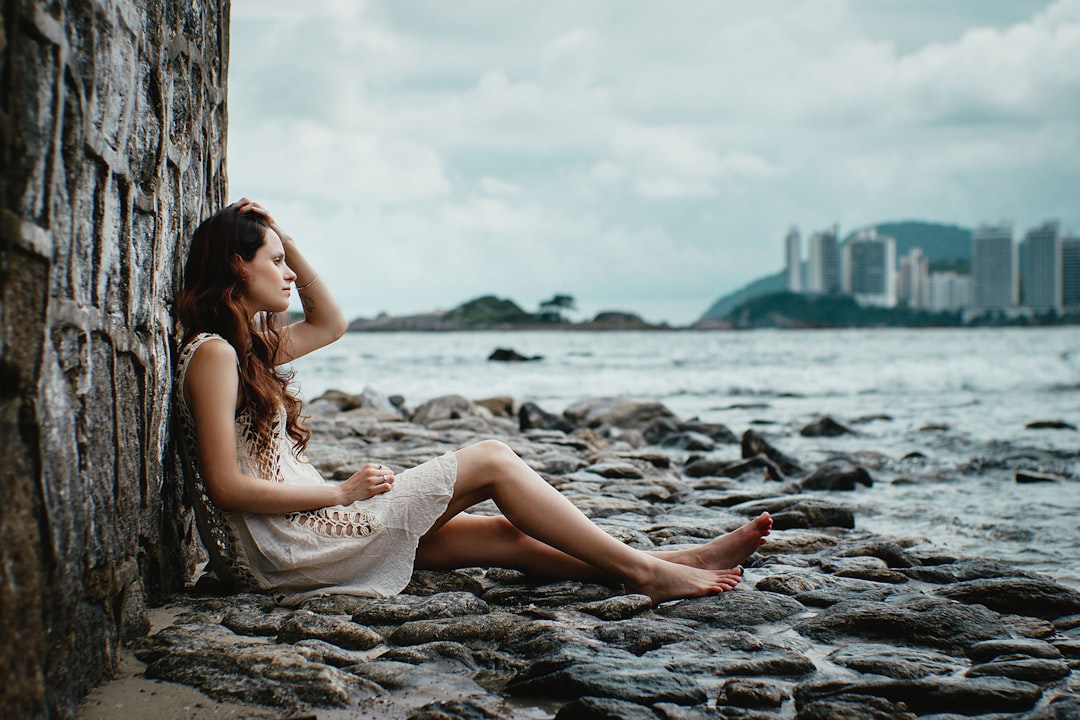 woman leaning on stone wall near body of water