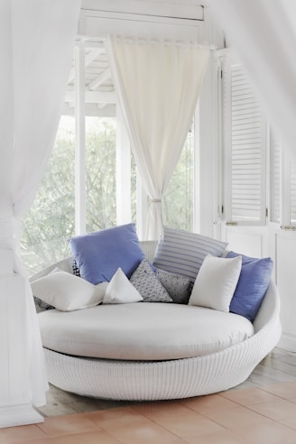 a clean white cuddle chair and throw pillows near window
