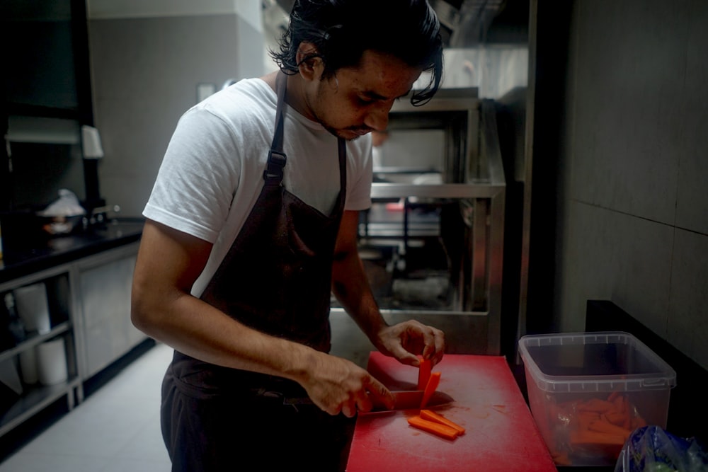 um homem cortando cenouras em uma tábua de corte em uma cozinha