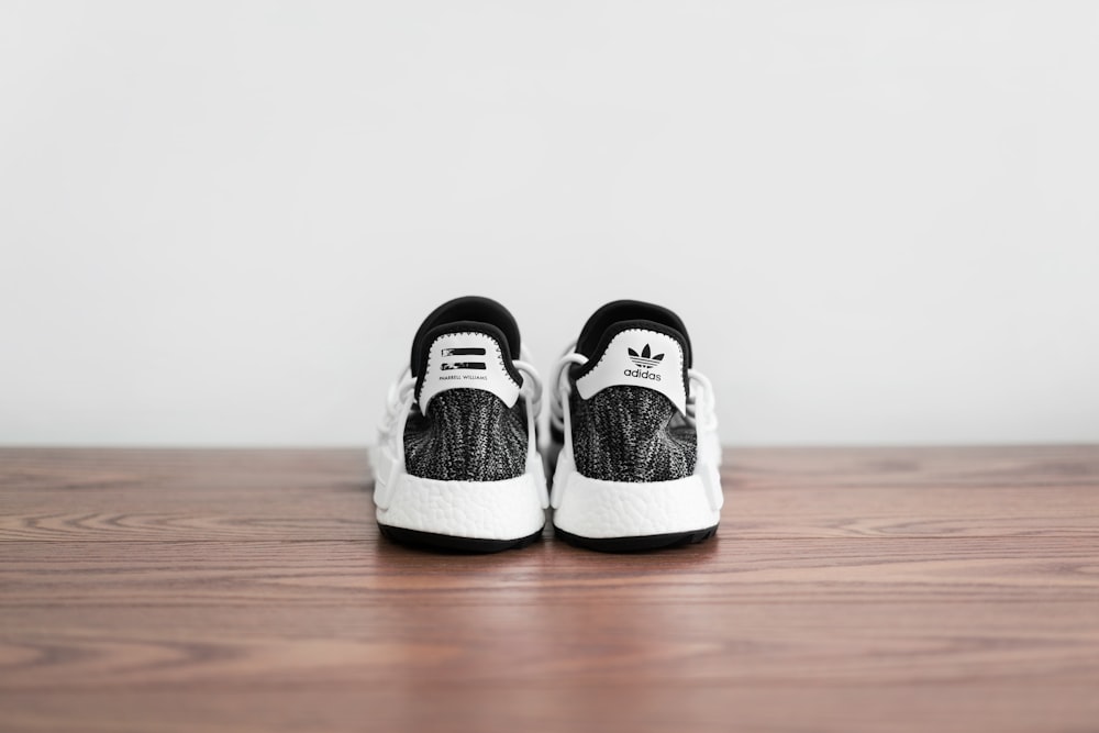 pair of white-and-black adidas shoes on wooden surface