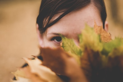 A close-up of a child’s curious eyes peeking through autumn leaves.