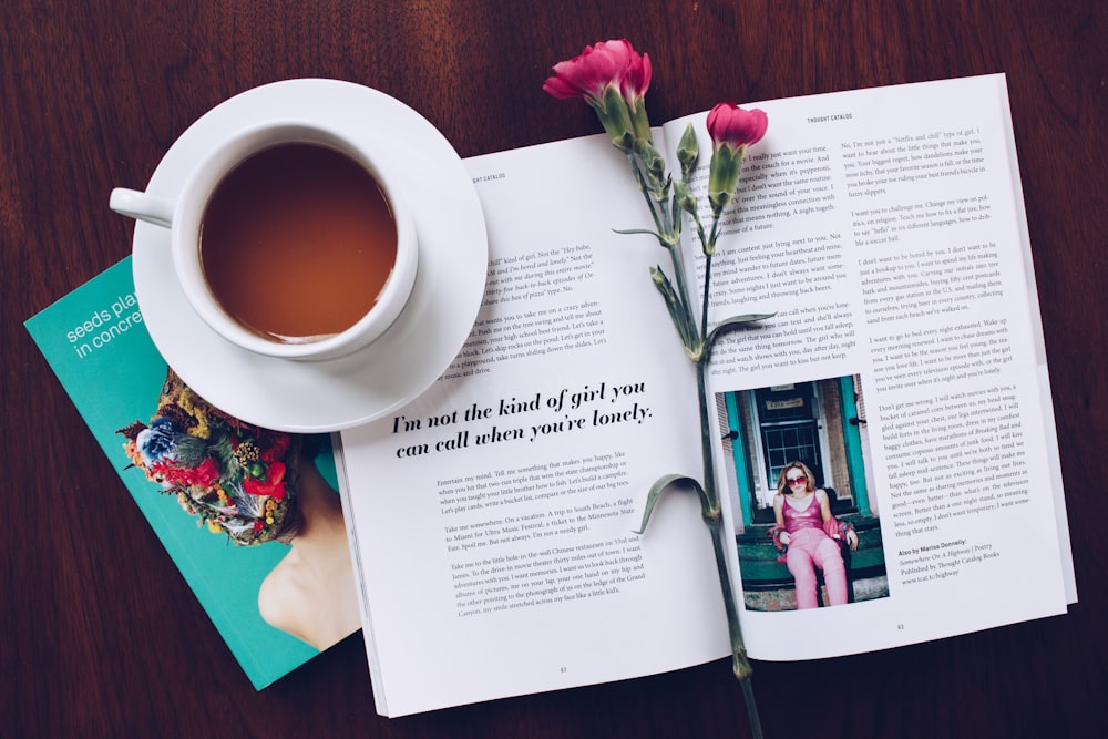 aufgeschlagenes Buch mit rosa Blume auf der Oberseite neben gefülltem Keramikbecher