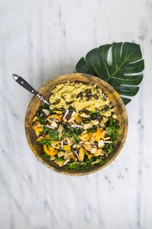 Close-up of a vibrant lunch bowl with fresh greens, avocado, and quinoa on a rustic wooden table.
