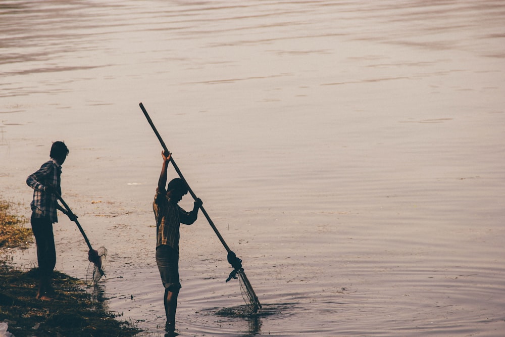 two men fishing on body of water at daytime